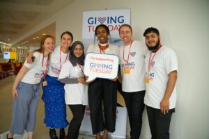 A group of six people wearing "Giving Tuesday" shirts stand together, smiling and holding a sign that says, "I'm supporting Giving Tuesday."