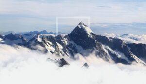 **Alt text:** Snow-capped mountain peaks emerge above a layer of clouds under a partly cloudy sky.