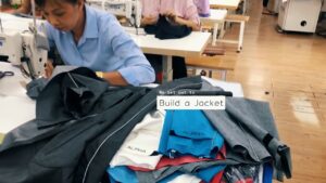 A woman in a blue shirt is sewing fabric at a workstation surrounded by colorful textile pieces with the words "We set out to Build a Jacket" overlaid on the image.