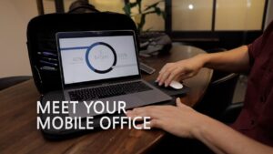 A person using a laptop inside a portable case on a wooden table with the text "Meet Your Mobile Office" displayed on the image.