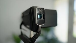 A close-up of a digital video camera with a prominent lens facing outward.