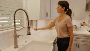 A woman in a kitchen adjusts a spring coil faucet above a white sink.