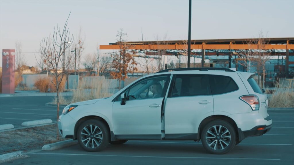 A white SUV is parked in an empty parking lot with its driver's side door open.