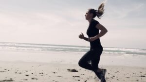 A person jogging along a sandy beach with the ocean in the background.