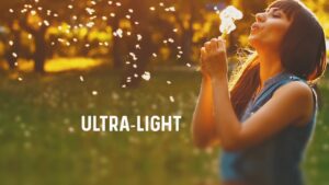 A person in a sunny field blows on a dandelion, with the word "ULTRA-LIGHT" written beside them.
