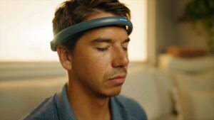 A man with closed eyes wearing a headband with a small blue light on the front.