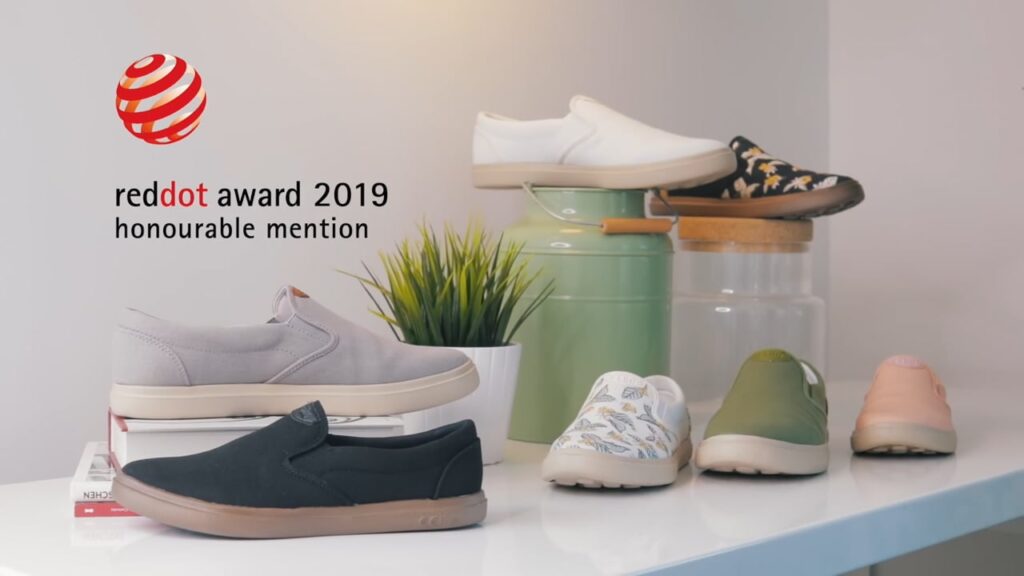 A display of various casual slip-on shoes alongside a plant, with a "reddot award 2019 honourable mention" sign.