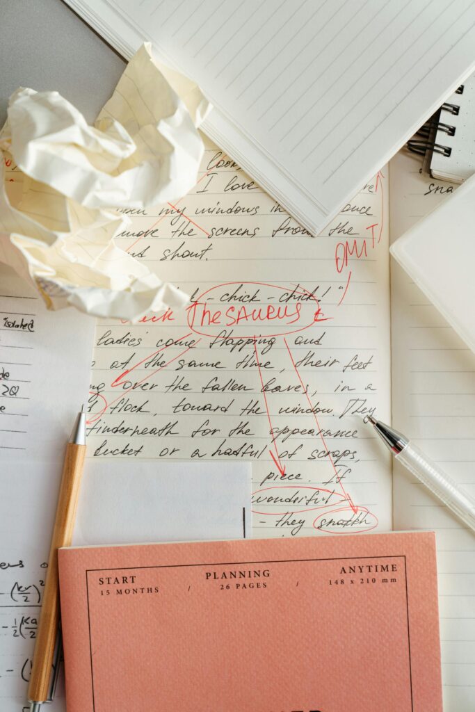 A messy desk with handwritten notes showing red editing marks, a crumpled paper, a notebook, and a planner labeled "Start Planning Anytime."