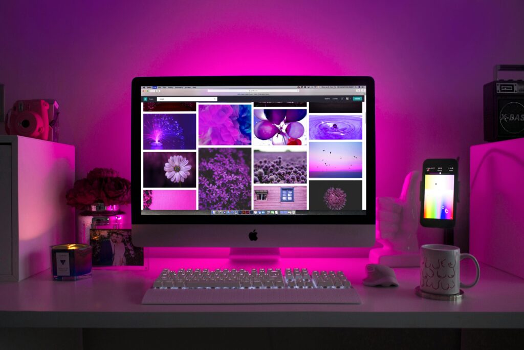 A desktop computer setup illuminated with pink lights, displaying various purple-themed images on the screen.