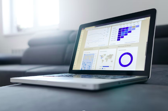 A laptop displaying various charts and graphs on its screen is placed on a dark sofa.