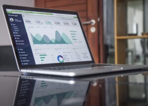 A laptop displaying various graphs and charts on its screen, sitting on a reflective table.