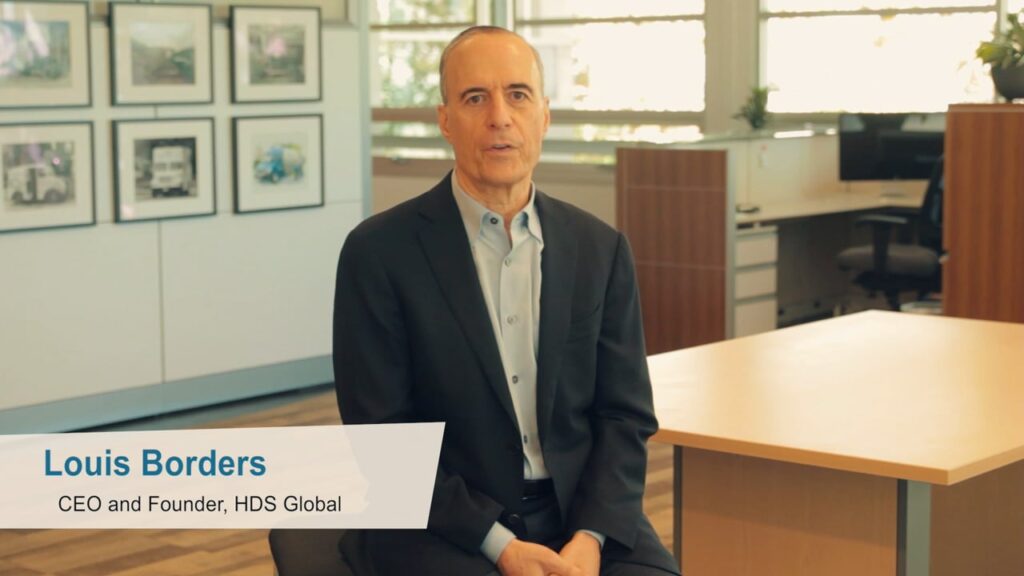 A man in a suit sits in a modern office space with artwork on the wall behind him.