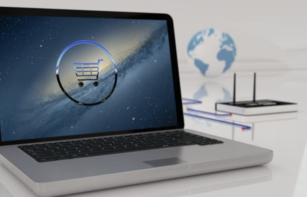 A laptop on a desk displays a shopping cart icon on its screen, with a globe and a router in the background.