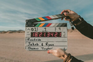 A person holds a film clapperboard in a desert setting, featuring labels "Roadside" and names "Jakob & Ryan."