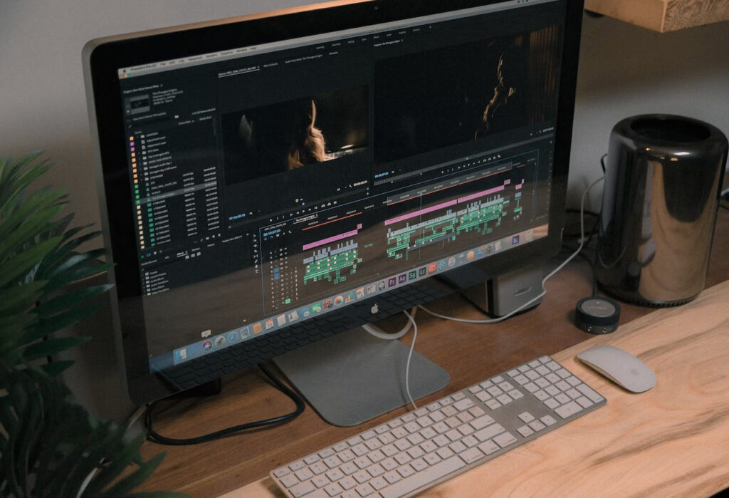 **Alt text:** A desktop computer displaying video editing software on its screen is placed on a wooden desk alongside a keyboard, mouse, and external hardware.