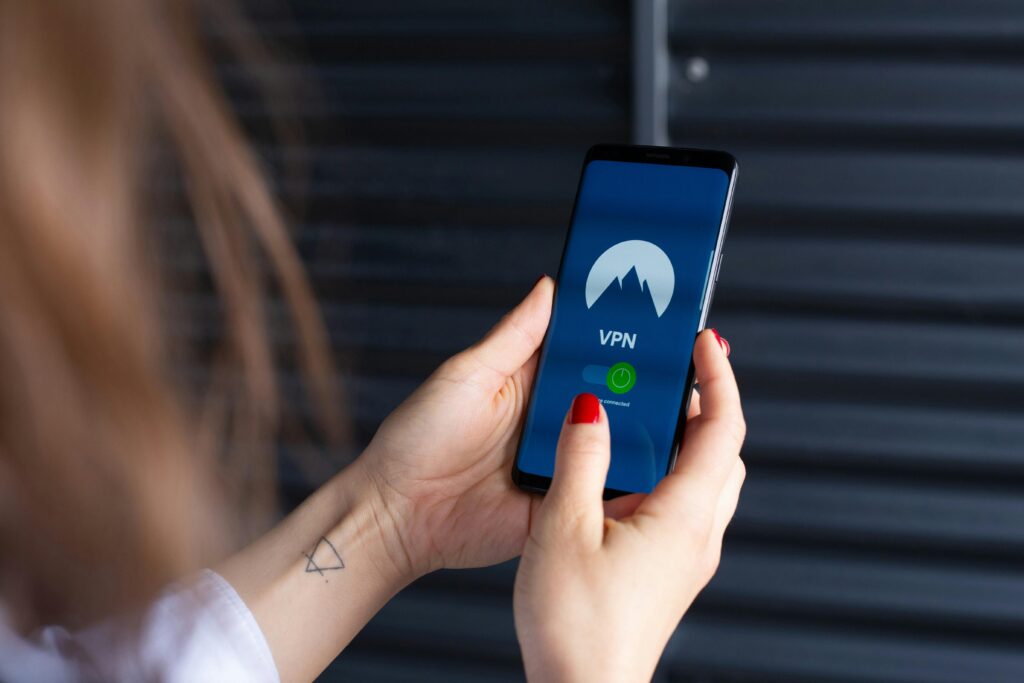 A person with red nail polish and a wrist tattoo holds a smartphone displaying a VPN app.
