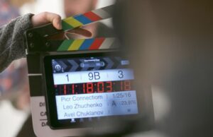 **Alt Text:** A clapperboard with colorful stripes being held by a person, displaying scene information and timing details.