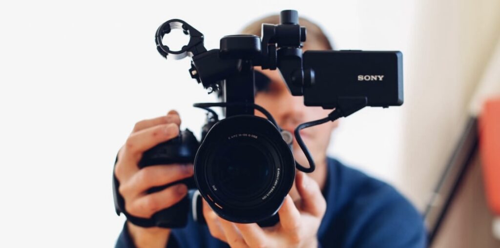 **Alt Text:** A person holding a Sony camera, looking directly into the lens, with the camera screen visible on the side.