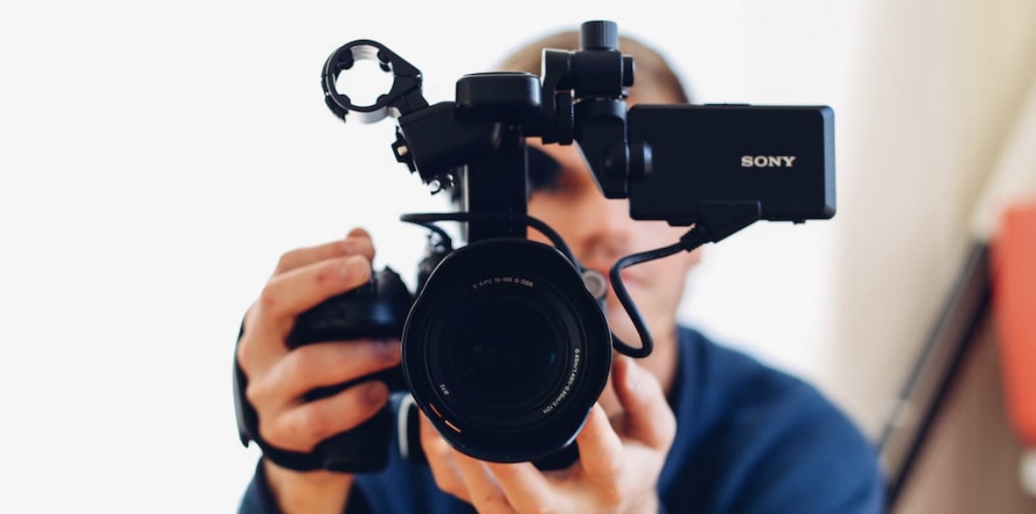 **Alt Text:** A person holding a Sony camera, looking directly into the lens, with the camera screen visible on the side.