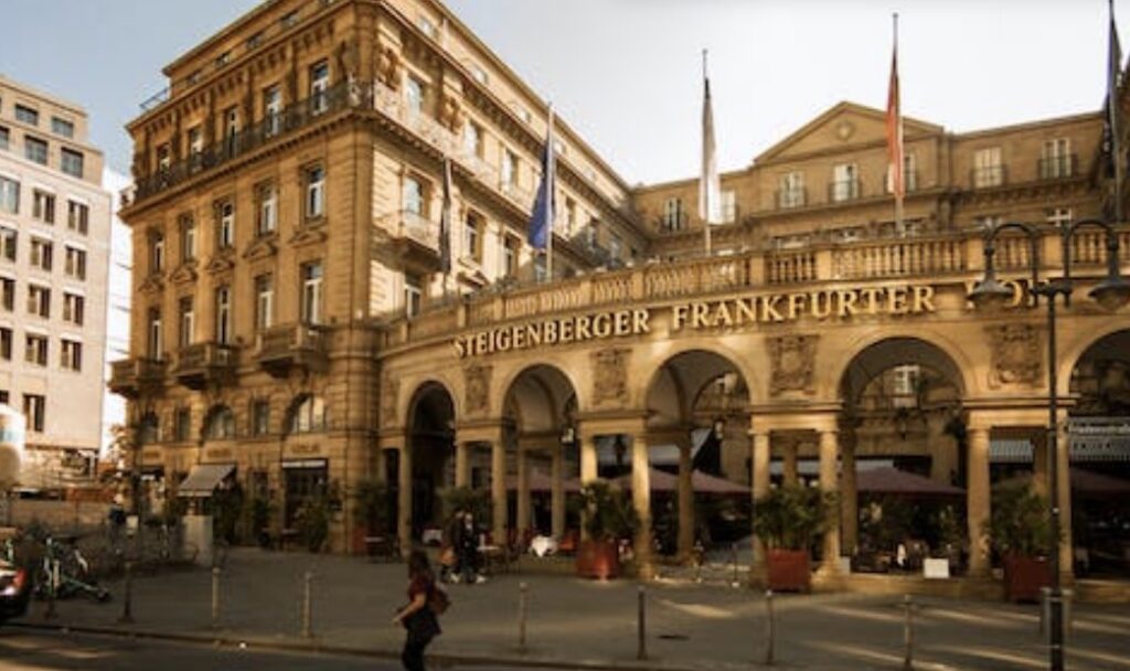A grand hotel building with arched entrances and flags, the Steigenberger Frankfurter Hof in Frankfurt.