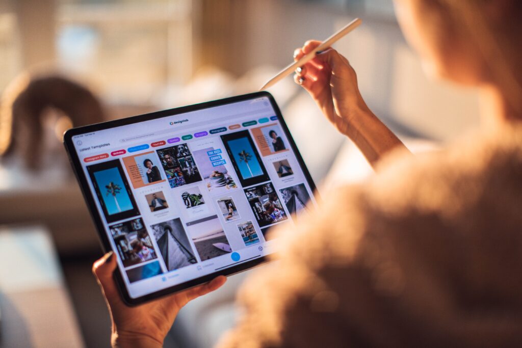 A person holds a tablet displaying a variety of design templates, using a stylus in their other hand.