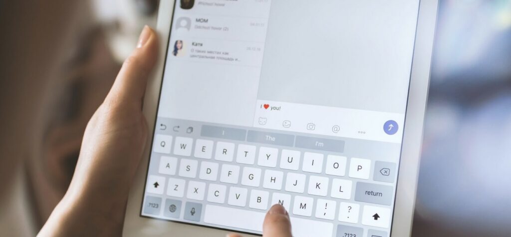 A person is typing a message saying "I ❤️ you!" on a tablet.