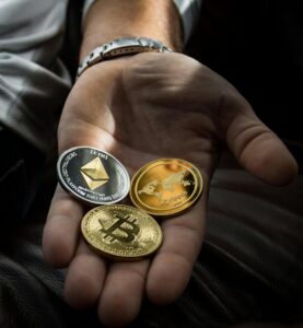 **Alt Text:** A hand holding three cryptocurrency coins: Ethereum, Ripple, and Bitcoin.