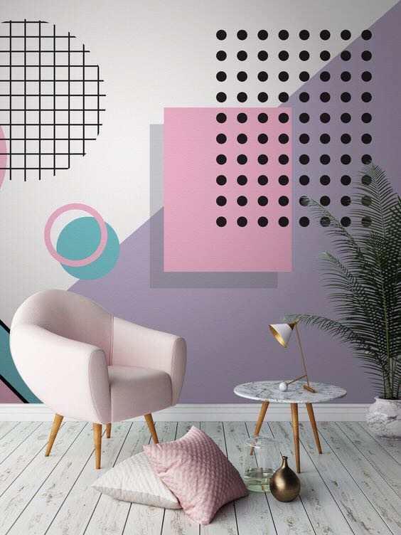 **Alt Text:** A modern living space with a pastel-colored geometric wall design, featuring a light pink armchair, a small marble side table, and decorative cushions on a wooden floor.