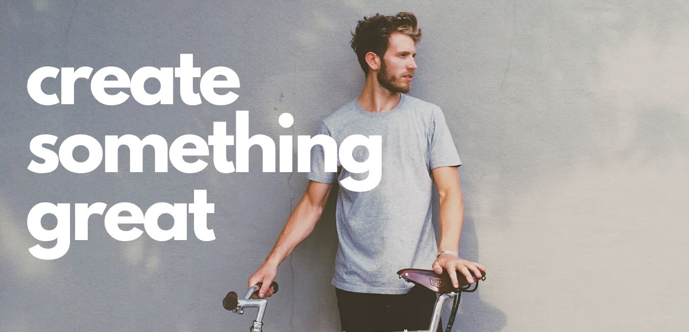A man in a gray T-shirt stands with a bicycle against a wall with the words "create something great."