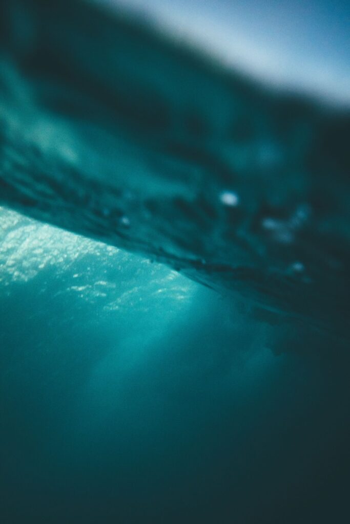 **Alt text:** A blurred underwater view with teal-colored water and sunlight filtering through from above.