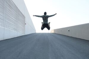 **Alt text:** A person in a hoodie jumps with arms outstretched on an ascending asphalt pathway between two walls.