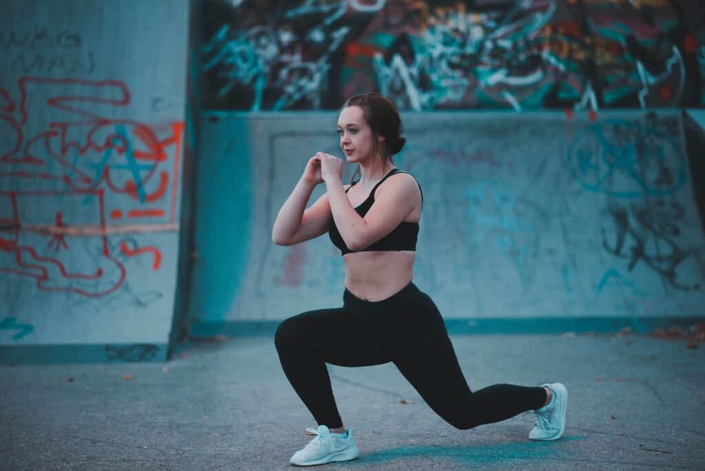 A person in athletic wear performs a lunge exercise in front of a graffiti-covered wall.