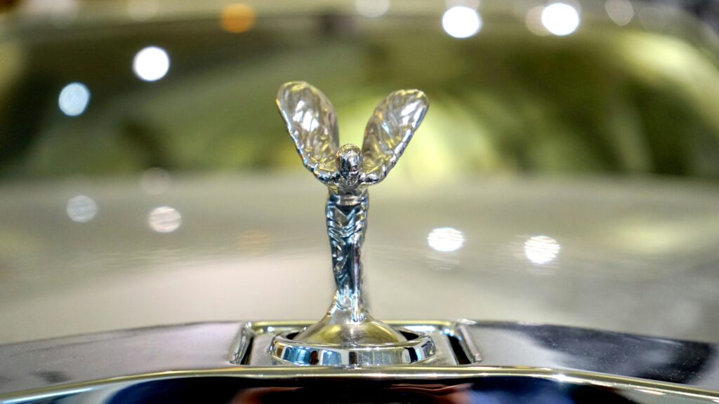 A close-up image of a silver winged figure hood ornament on a car.