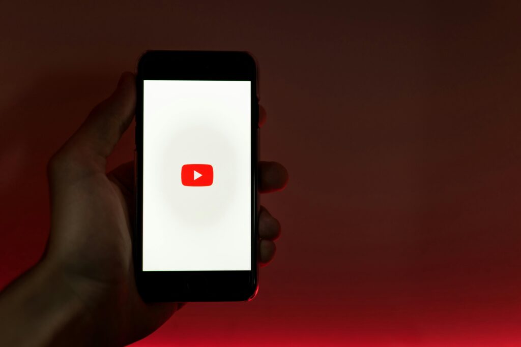 A person holds a smartphone displaying the YouTube logo against a dark background.