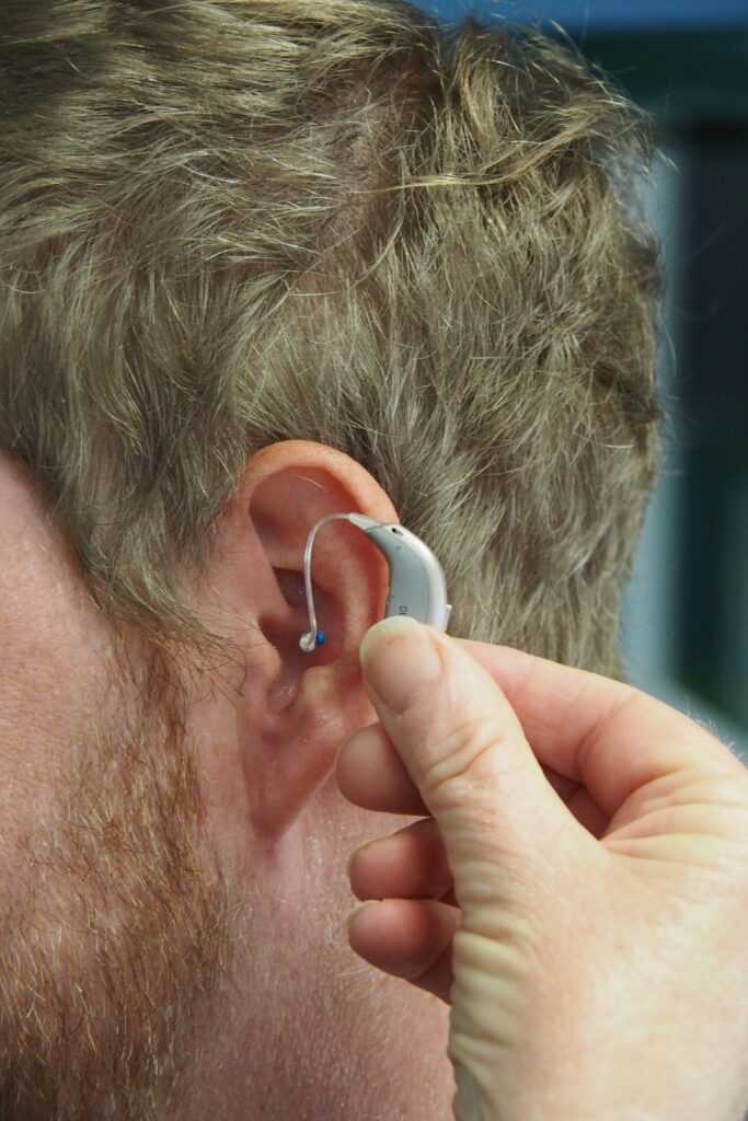 **Alt Text:** A hand is fitting a hearing aid behind a man's ear.