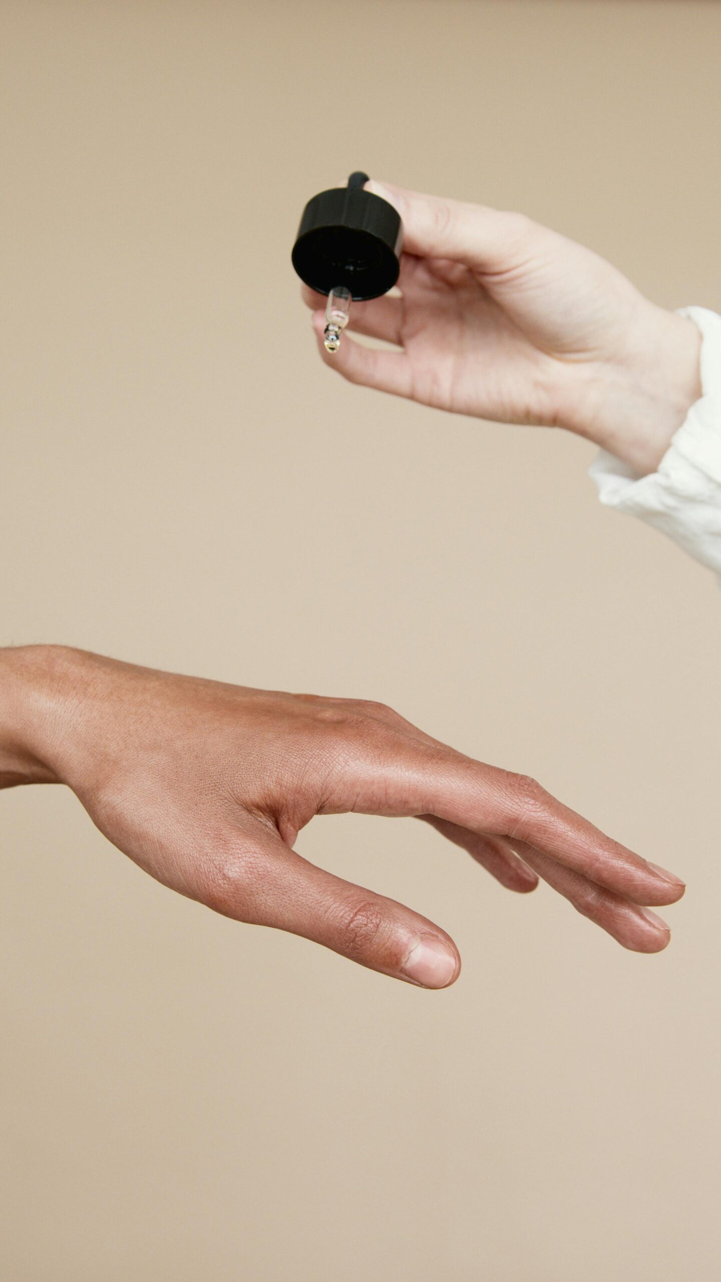 A hand is holding a dropper above another hand as if about to apply a liquid.
