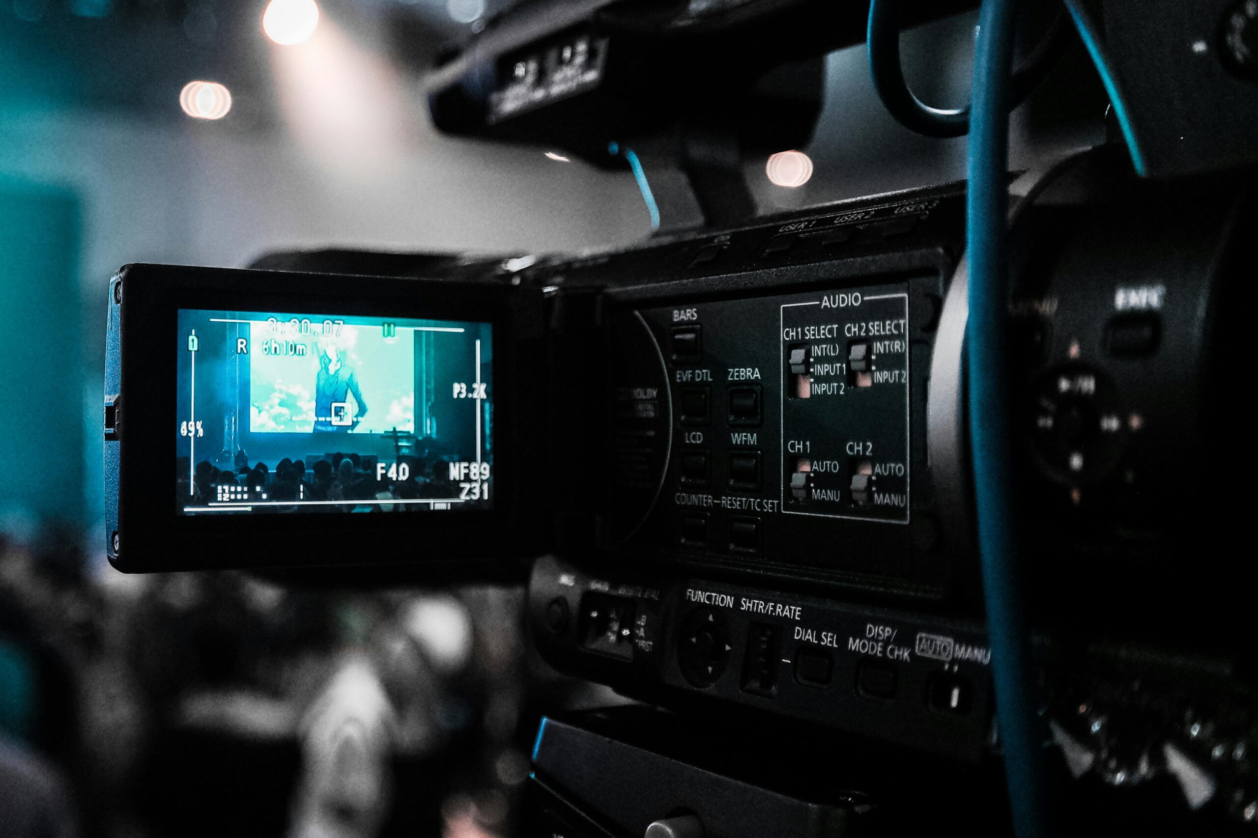 **Alt text:** A video camera capturing a live event, with its screen showing the audience and stage.