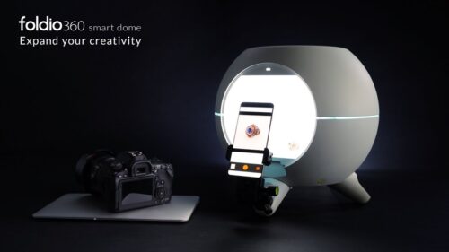 **Alt text:** A Foldio360 smart dome is shown next to a camera and a smartphone capturing an image inside the dome.