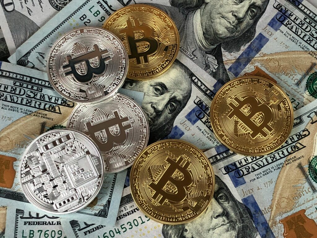 **Alt Text:** Several gold and silver Bitcoin tokens are scattered on top of US dollar bills.