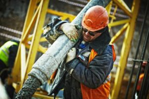 A construction worker wearing a hard hat and sunglasses operates a concrete pouring hose on a construction site.