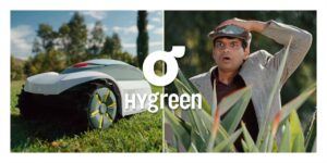 "A man looking astonished next to a robotic lawn mower on grass with the label 'Hygreen' in the center."