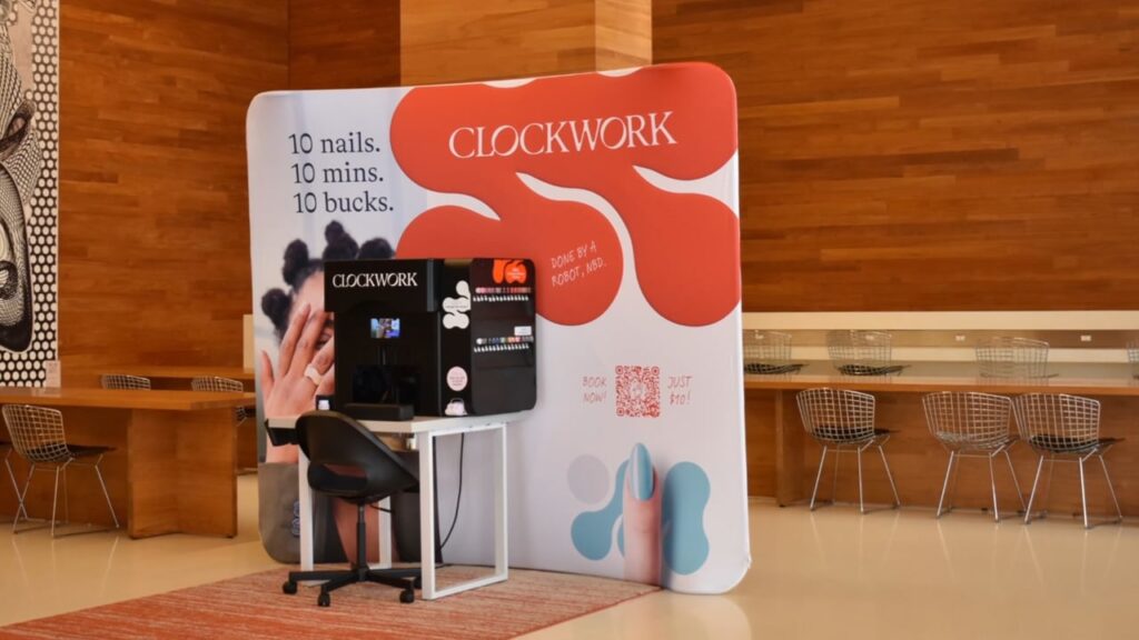 A Clockwork automated nail painting booth set up in a modern space with wooden walls and metal chairs.