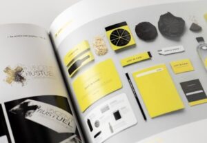 **Alt Text:** An open magazine displaying pages featuring a collection of branding materials, such as business cards, envelopes, and notebooks, primarily in yellow and black colors.