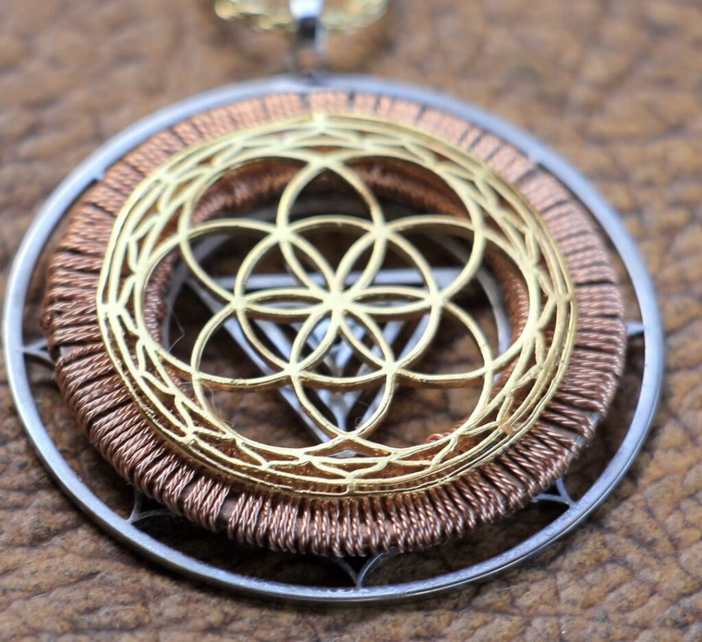 **Alt Text:** A close-up of a pendant featuring intricate patterns made of gold and copper wire in concentric circular designs.
