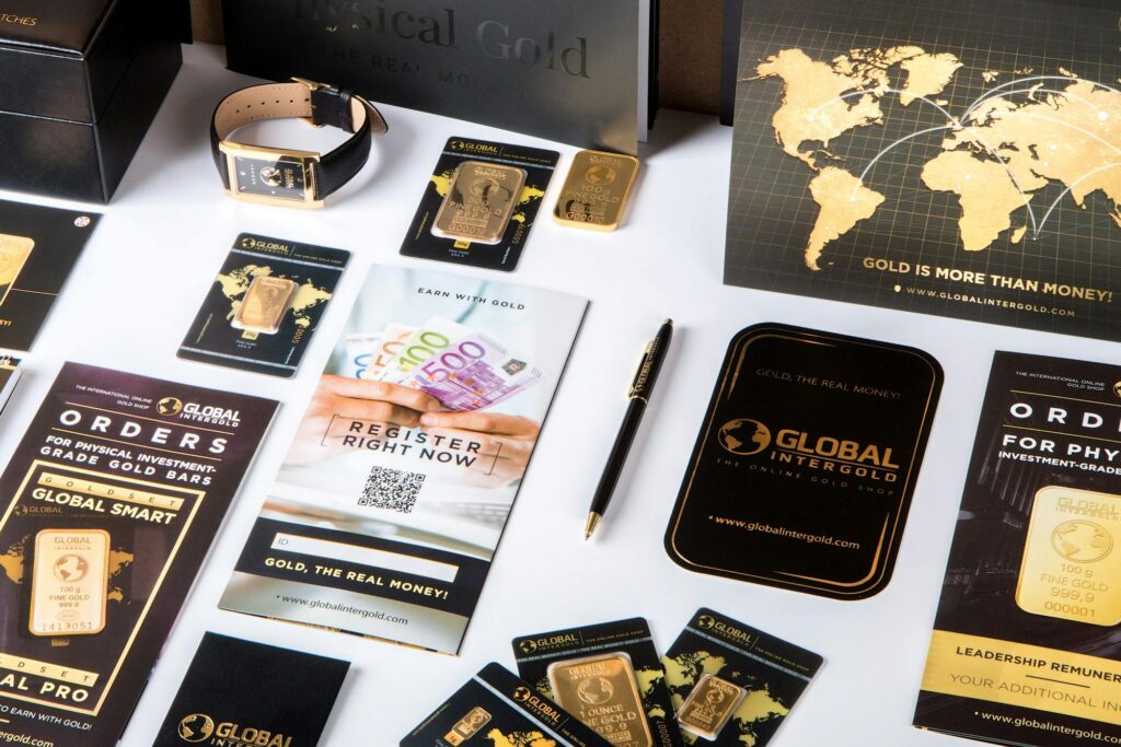A display of Global Intergold promotional materials, including brochures, a watch, gold bars, a pen, and a map-themed card.