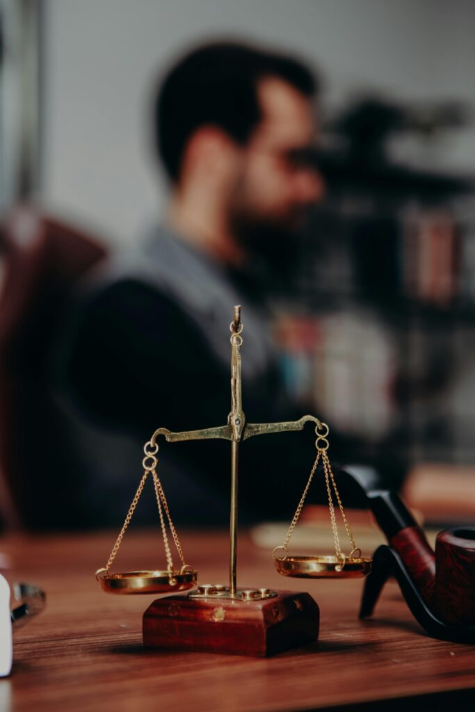 A close-up of a brass balance scale on a wooden desk, with a blurred person in the background.