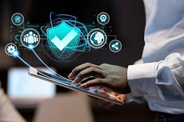 A person using a tablet with digital icons representing technology and security, including a shield with a checkmark and various gear symbols, hovering above the device.