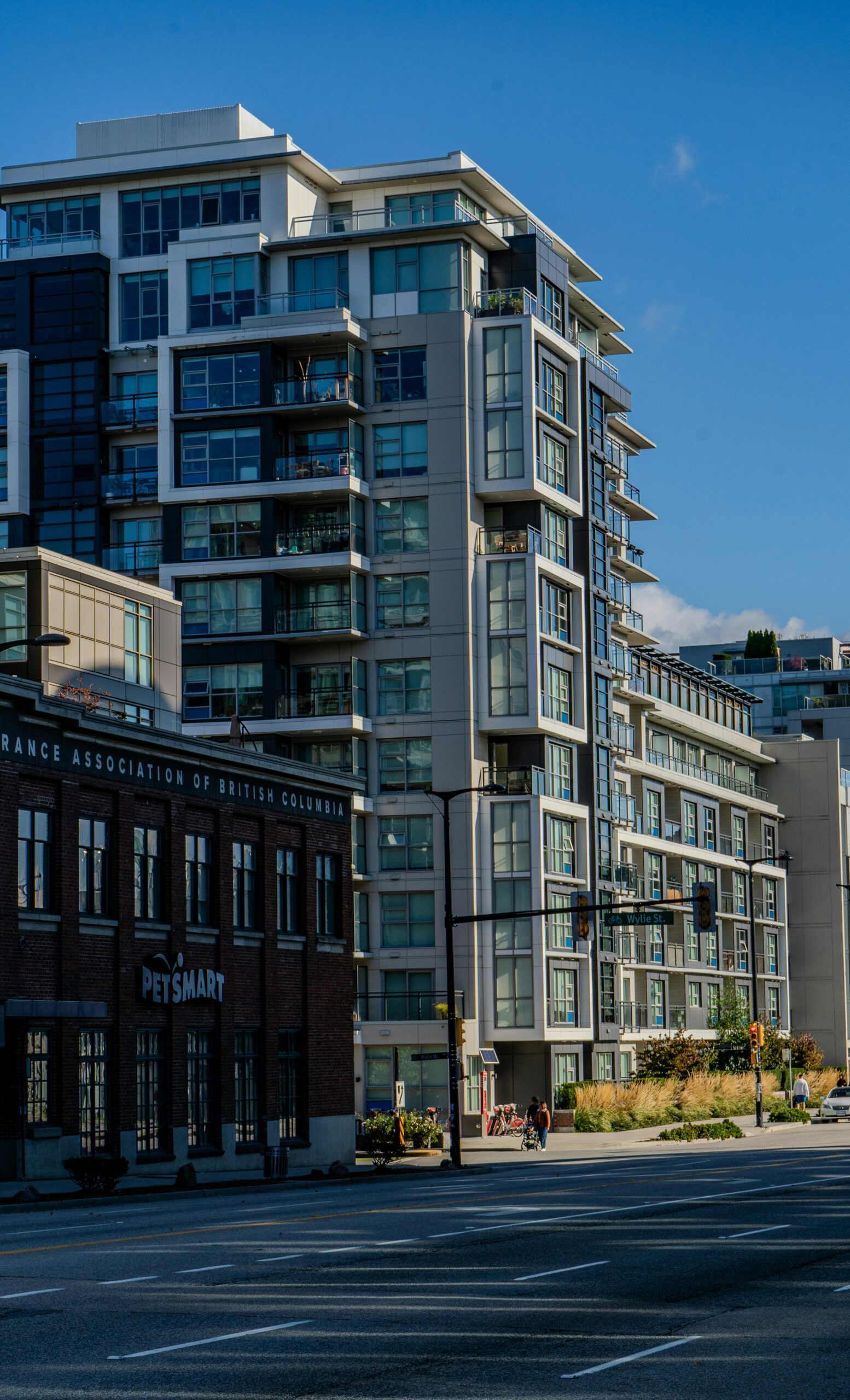A modern apartment building with large windows stands next to a brick PetSmart store on a sunny day.