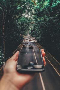 A hand holding a smartphone in front of a road lined with trees, with the phone screen seamlessly blending into the real scene of cars driving on the road.