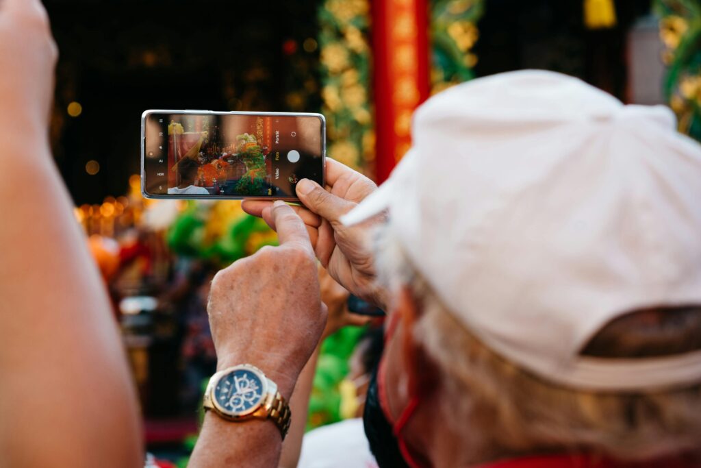 A person wearing a white cap takes a photo of a colorful lion dance with a smartphone.
